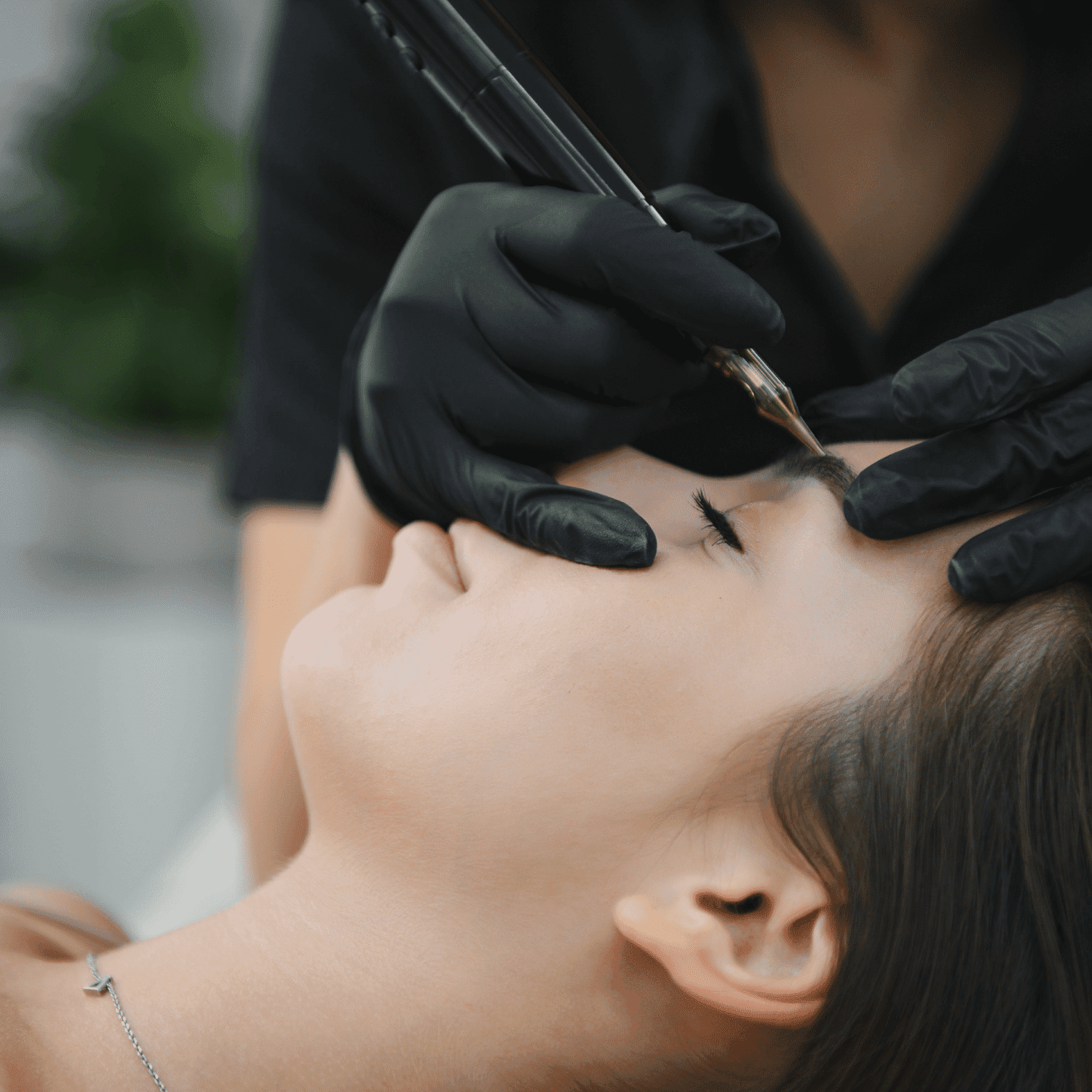 Eyebrow tattoo procedure in progress with technician wearing black gloves.
